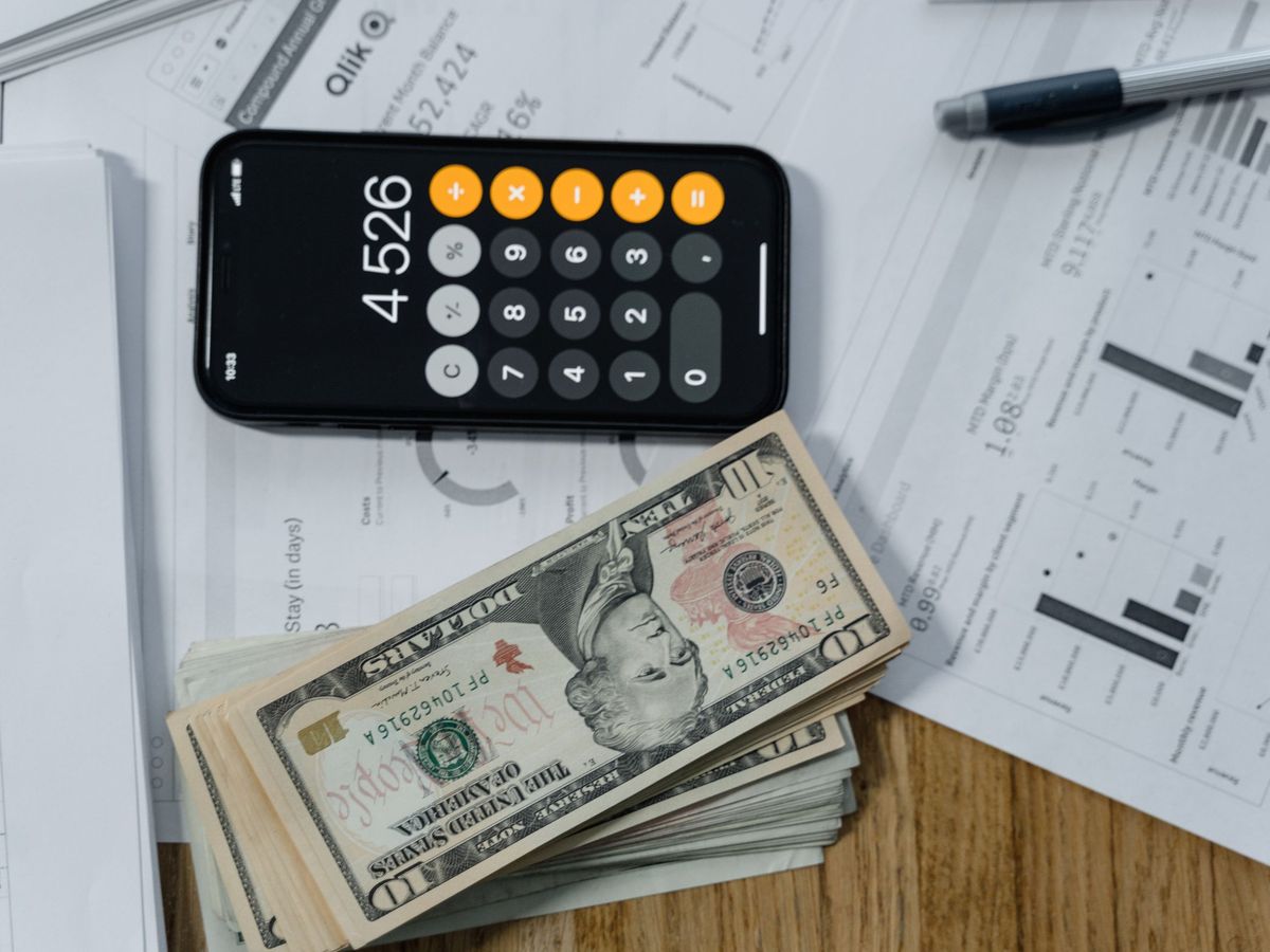 A calculator, banknotes and printed financial documents arranged on a desk